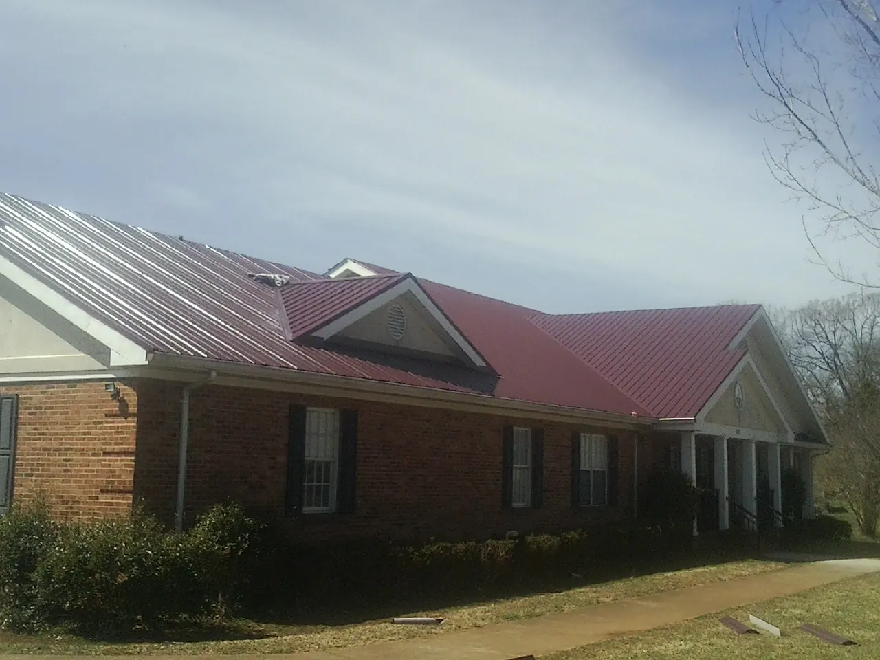 Red metal roof with gabled entries on a long brick building, from a Hail Damage Roof Repair job in Cashmere