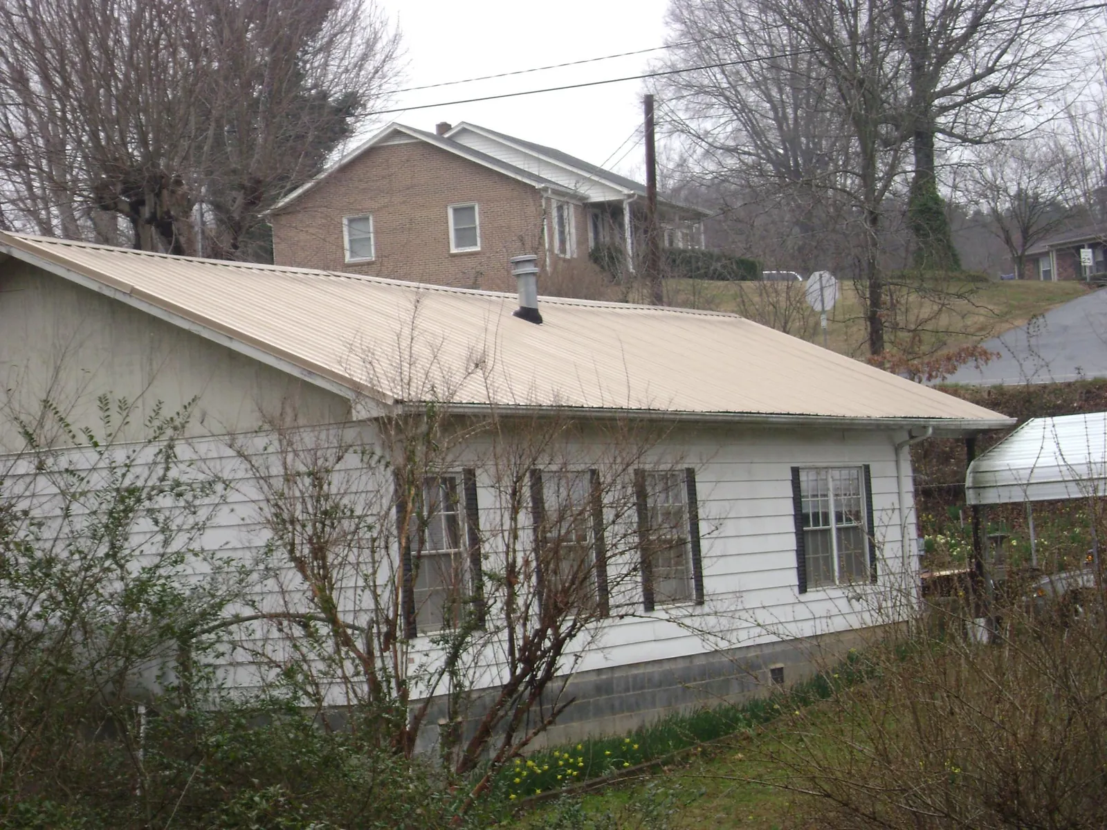 Tan metal roof on a white sided house set into a hillside — Commercial Roofing by Roofing Brothers in Cashmere